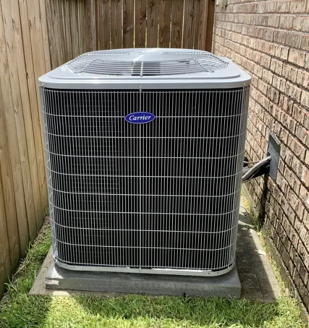 A Carrier condenser installed on its pad between a cedar fence and a brick wall