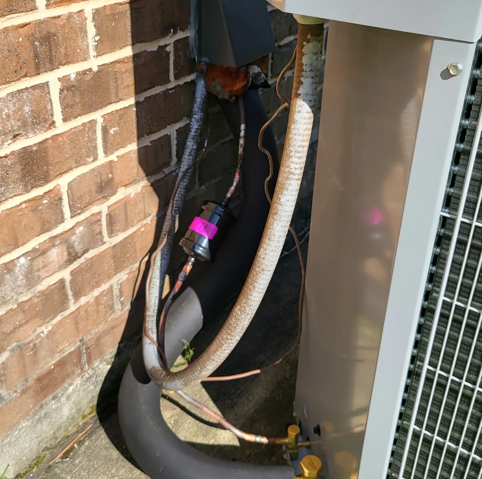 Refrigerant lines, a disconnect box and service valves beside an outdoor unit against a brick wall